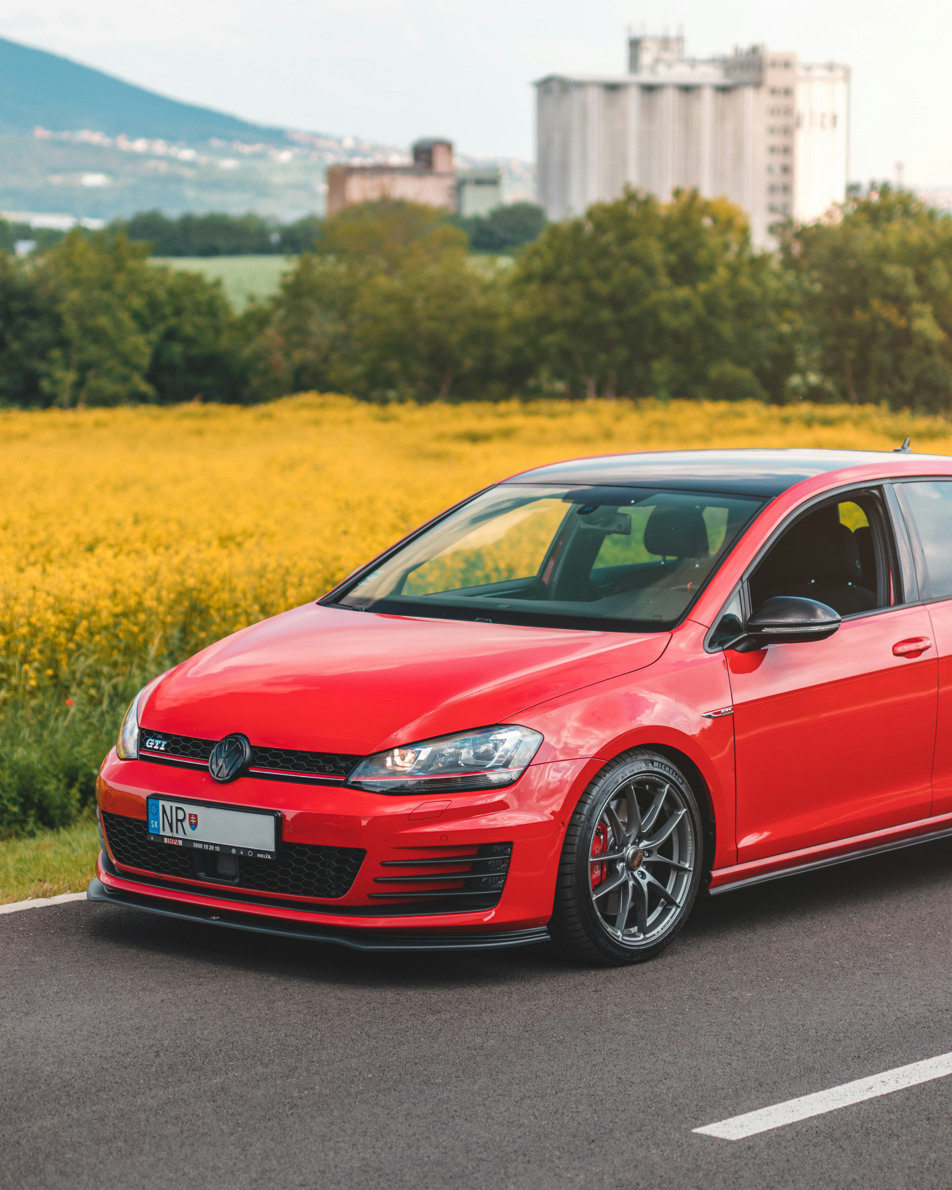 Lowered red Volkswagen GTI with aftermarket wheels and carbon splitter on a country road